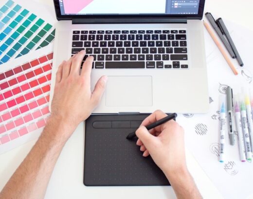 Designer arbeitet mit Laptop und Grafiktablett zwischen Farbmustern und Stiften